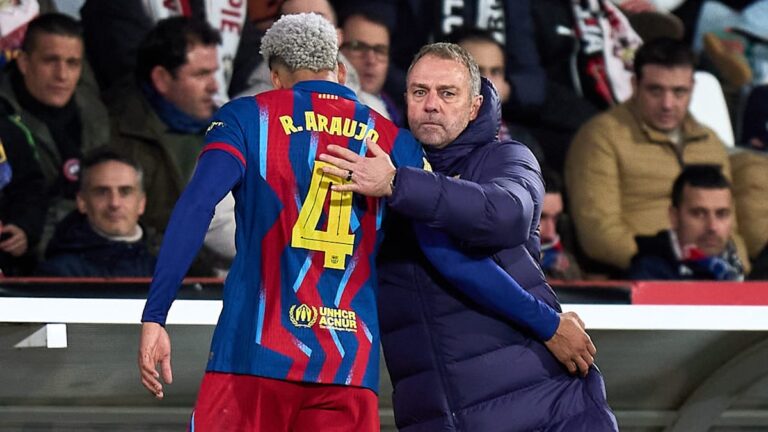 Hansi Flick steht nachdenklich an der Seitenlinie des FC Barcelona, im Hintergrund trainiert Ronald Araujo.