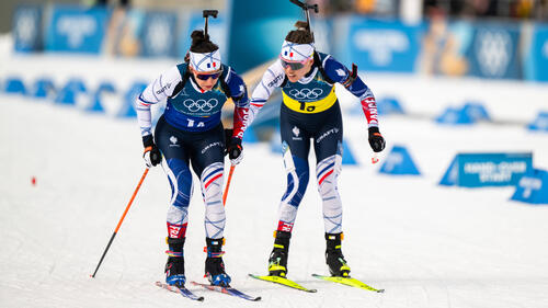 Julia Simon überquert jubelnd mit der französischen Flagge die Ziellinie beim Biathlon-Staffelsieg