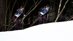 Frida Karlsson jubelt im Zielbereich über ihre Goldmedaille, während im Hintergrund enttäuschte Konkurrentinnen zu sehen sind.