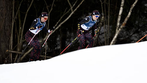 Frida Karlsson jubelt im Zielbereich über ihre Goldmedaille, während im Hintergrund enttäuschte Konkurrentinnen zu sehen sind.