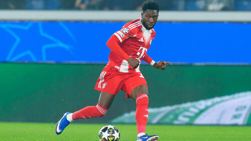Alphonso Davies im Trikot des FC Bayern München blickt nachdenklich auf dem Spielfeld.