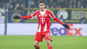 Jamal Musiala im Trikot des FC Bayern München mit leicht schmerzverzerrtem Gesicht auf dem Rasen