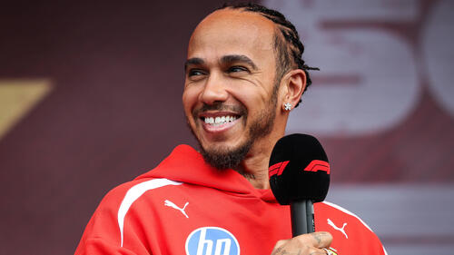 Lewis Hamilton im roten Ferrari-Rennanzug lächelnd in der Boxengasse von Melbourne