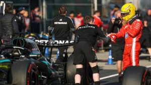 Lewis Hamilton im Ferrari-Rennanzug hockt in der Boxengasse und begutachtet ein Formel-1-Auto