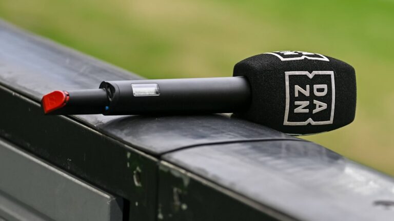 Ein American Football liegt auf dem Rasen eines Stadions, im Hintergrund unscharfe Tribünen – Symbolbild für NFL-Übertragungsrechte.