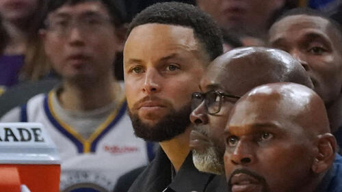 Stephen Curry in Zivilkleidung auf der Bank der Golden State Warriors während eines Spiels