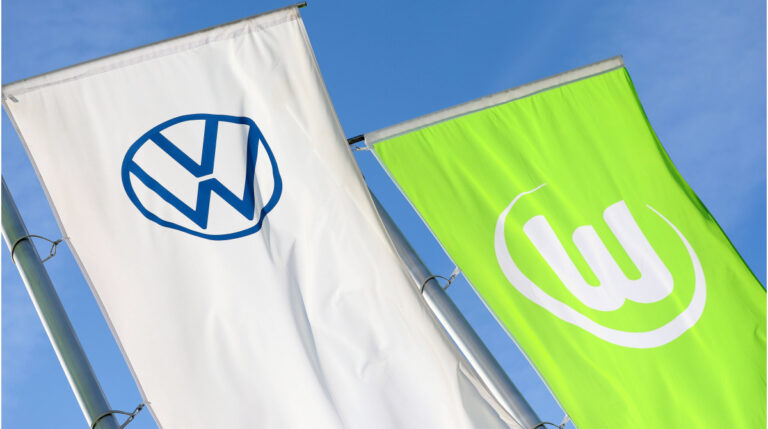 Das Logo des VfL Wolfsburg neben dem VW-Emblem vor der Volkswagen Arena in der Autostadt.