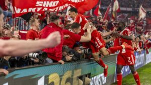 Fans des FC Bayern München jubeln mit Schals in der Allianz Arena vor der Südkurve