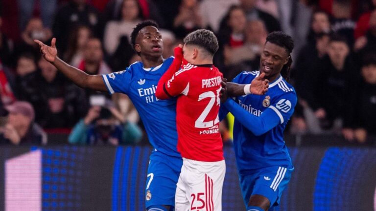 Ein Schiedsrichter zeigt einem Fußballspieler, der sich das Trikot über den Mund zieht, die Rote Karte.