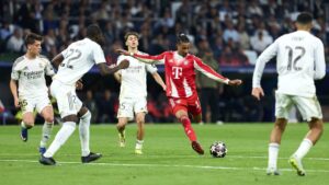 Michael Olise im Trikot des FC Bayern München dribbelt mit dem Ball auf dem Spielfeld.