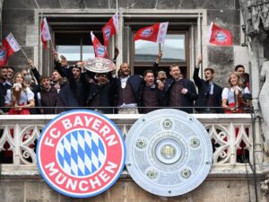 Die Spieler des FC Bayern München jubeln in Tracht mit der Meisterschale auf dem Rathaus-Balkon.