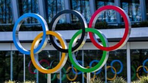 Die olympischen Ringe neben einer belarussischen Flagge vor einem großen internationalen Sportstadion