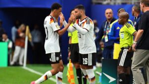Deniz Undav jubelt im DFB-Trikot, während Jamal Musiala nachdenklich auf der Ersatzbank sitzt.