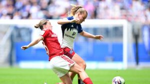 Ein Fußball auf dem Rasen der Frauen-Bundesliga, im Hintergrund verschwommene Umrisse eines Stadions.