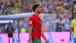 Achraf Hakimi im Trikot der marokkanischen Nationalmannschaft blickt mit ernster Miene auf das Spielfeld.