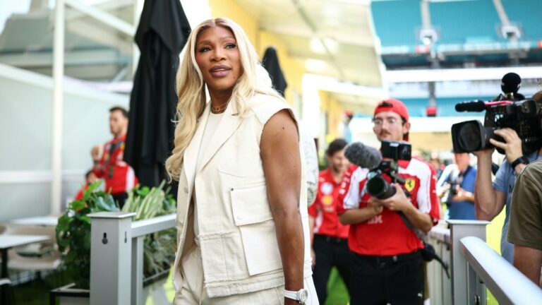 Serena Williams lacht im Tennis-Outfit auf einem Rasenplatz und hält ihren Tennisschläger