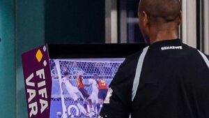 Ein Schiedsrichter greift sich ans Headset, während er bei einer Weltmeisterschaft auf den Video-Monitor schaut.