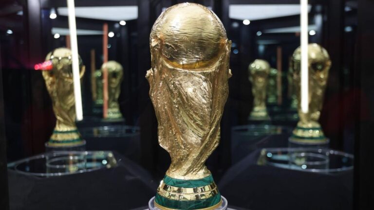 Der FIFA-WM-Pokal vor einer Stadion-Anzeigetafel mit dem offiziellen Logo der WM 2026