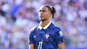 Michael Olise im Trikot des FC Bayern München blickt ernst und nachdenklich auf das Spielfeld.