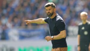 Ein Fußball liegt auf dem Rasen eines Bundesliga-Stadions, im Hintergrund sind Tribünen zu sehen