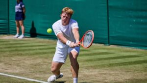 Ein junger deutscher Tennisspieler schlägt auf dem Rasen von Wimbledon einen Aufschlag.
