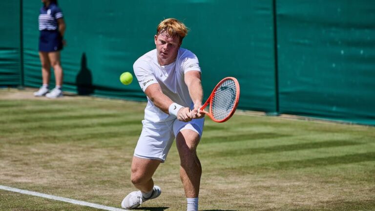 Ein junger deutscher Tennisspieler schlägt auf dem Rasen von Wimbledon einen Aufschlag.