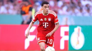 Jamal Musiala im Trikot des FC Bayern München blickt nachdenklich auf das Spielfeld