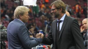 Oliver Kahn blickt ernst und nachdenklich, während im Hintergrund Bundestrainer Jürgen Klopp gestikuliert.