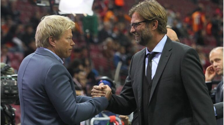 Oliver Kahn blickt ernst und nachdenklich, während im Hintergrund Bundestrainer Jürgen Klopp gestikuliert.