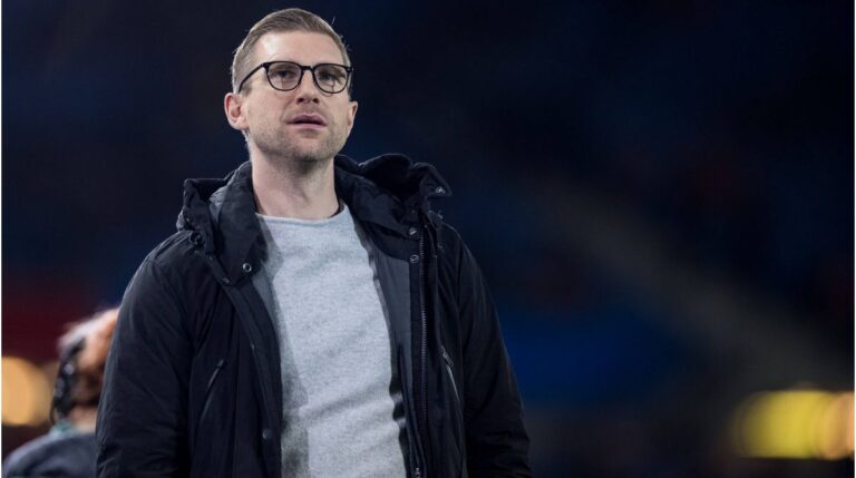 Per Mertesacker im Anzug blickt fokussiert, im Hintergrund das Logo des Deutschen Fußball-Bundes