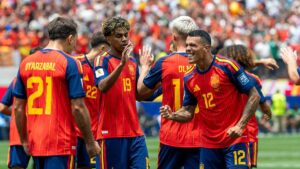Spanische Nationalspieler bejubeln ein Tor bei der WM, während enttäuschte Österreicher im Hintergrund stehen.