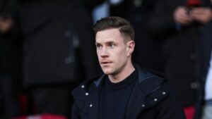 Marc-André ter Stegen präsentiert lächelnd das grüne Torwarttrikot von Ajax Amsterdam mit der Rückennummer eins